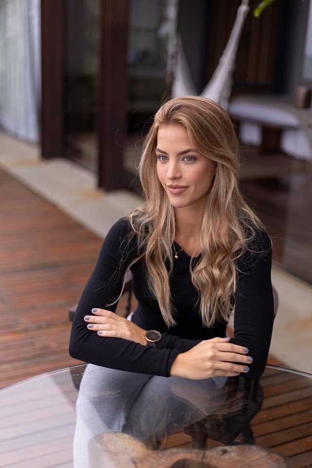 Carol Aszmann sentada a uma mesa de vidro, bracos cruzados